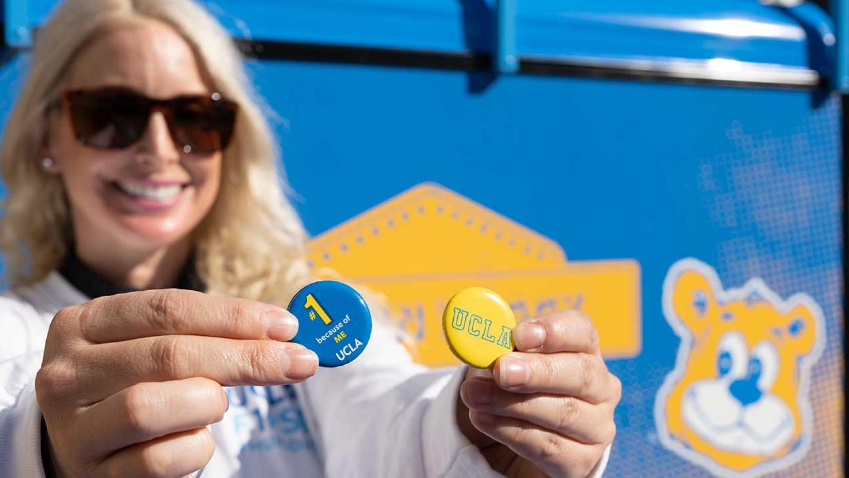 A smiling UCLA employee holds up UCLA is #1 pins at First Thursdays event 
