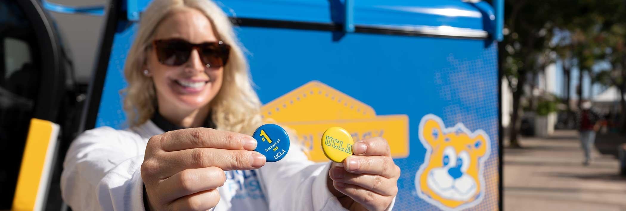 A smiling UCLA employee holds up UCLA is #1 pins at First Thursdays event 