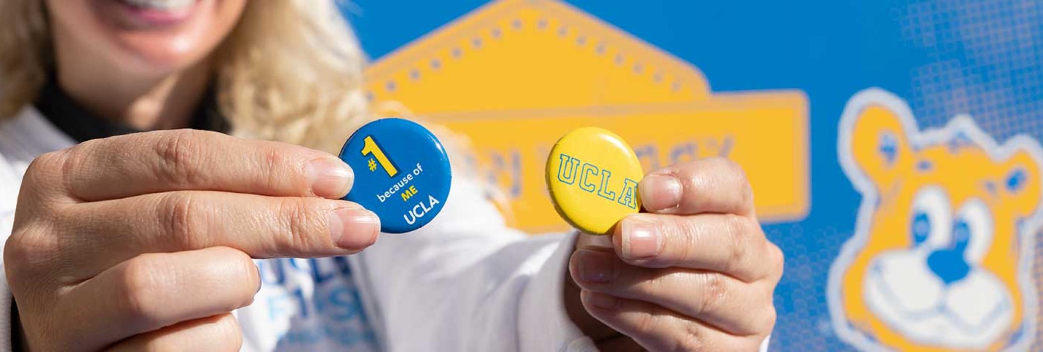 A smiling UCLA employee holds up UCLA #1 pins at a First Thursdays event